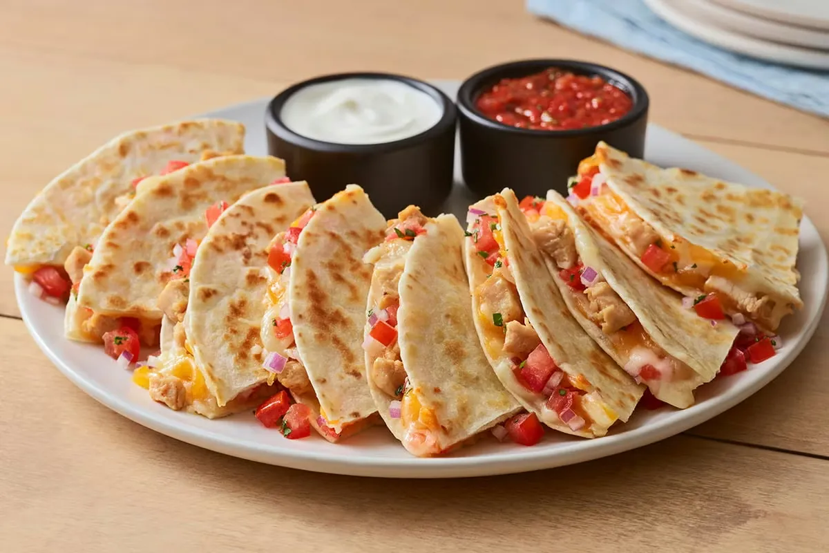 Golden grilled chicken quesadillas cut into triangles and served on a white plate with dipping sauces.