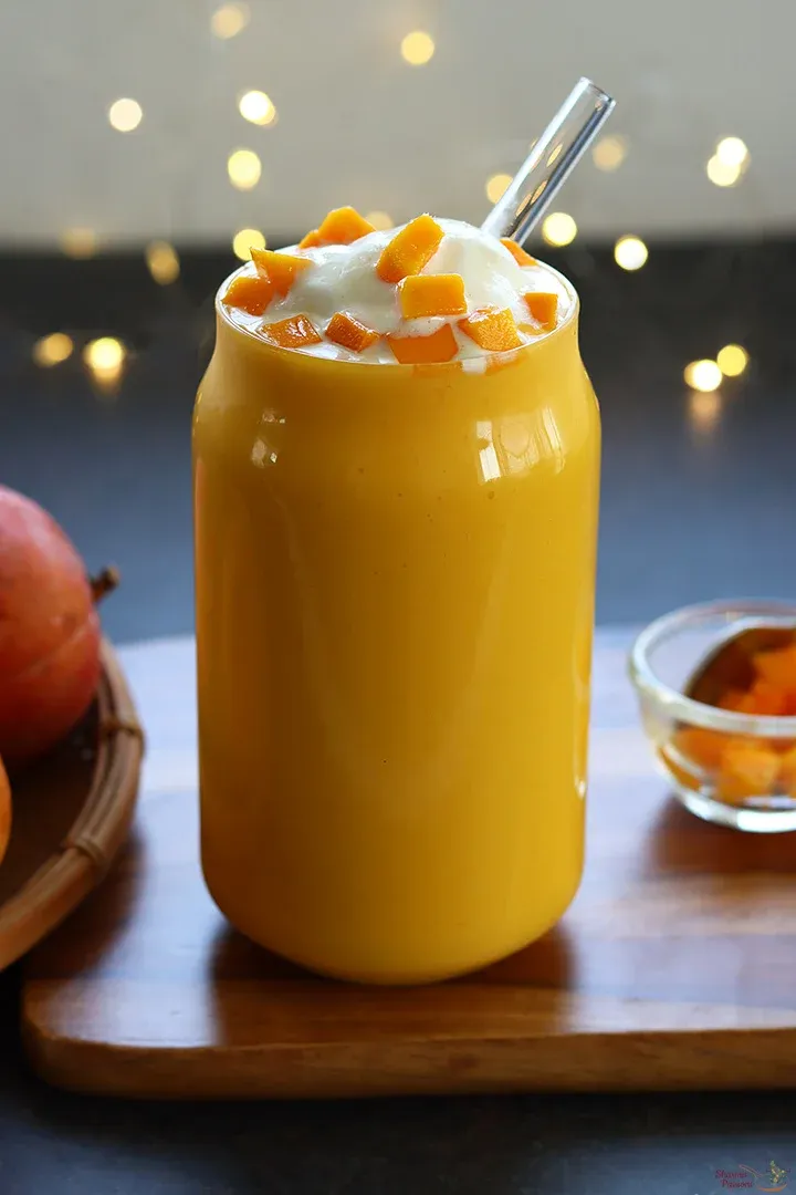 Glass of mango shake topped with cream and mango pieces