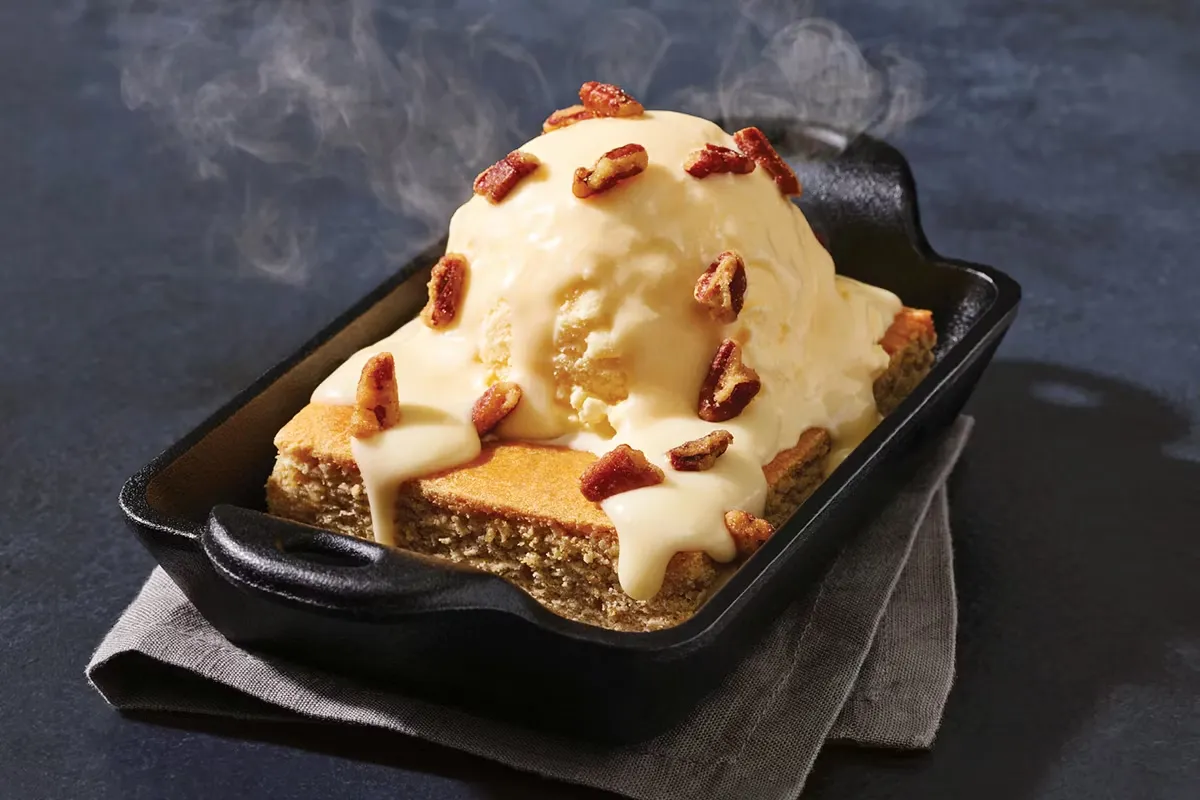 Golden blondie dessert with pecans, topped with melting ice cream and sweet syrup drizzle.
